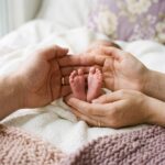 Adult hands cupped around a newborn baby feet on a knitted blanket